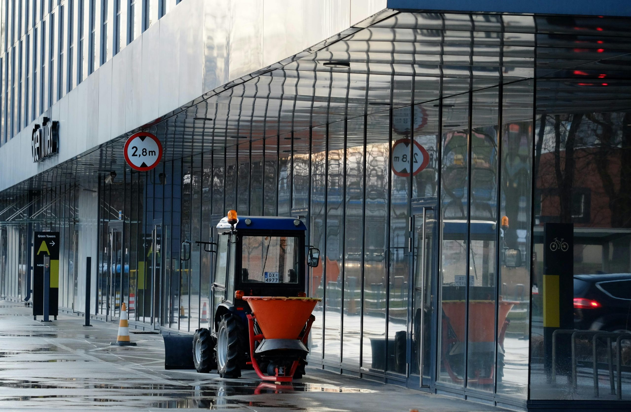 A small tractor outside a modern building with reflective glass.